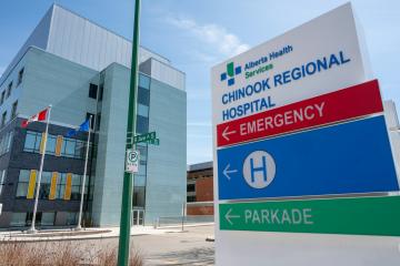 A large outdoor sign for the Chinook Regional Hospital, displaying directions to the Emergency entrance, Hospital main entrance (H), and Parkade, with the hospital building visible in the background.