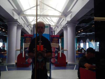 A man taking a mirror selfie inside a science museum exhibit hall featuring white columns, a high truss ceiling, and displays labeled "BODY TYPES".