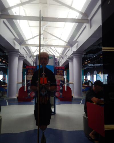 A man taking a mirror selfie inside a science museum exhibit hall featuring white columns, a high truss ceiling, and displays labeled "BODY TYPES".