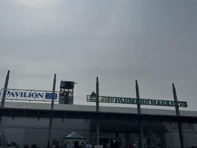 The image shows the exterior of a large market building with a sign reading "HALIFAX SEAPORT FARMERS' MARKET" and another sign for "PAVILION 23", with people walking in front on a paved area.