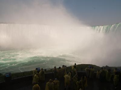 A panoramic view from an outdoor observation deck showing a massive waterfall with a large crowd of people wearing yellow rain ponchos.