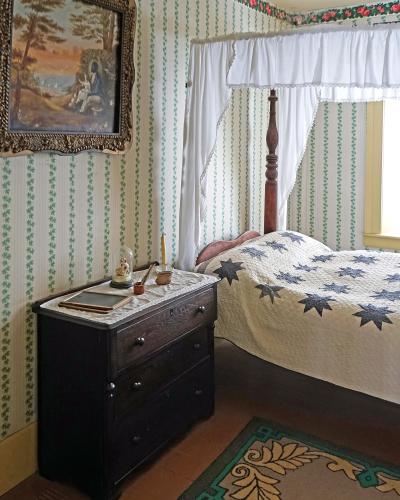 An interior bedroom scene featuring a four-poster bed with a star-patterned quilt, a dark wooden dresser, and walls covered in green and white striped wallpaper with a floral border.