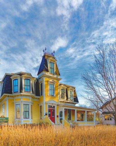 A yellow Victorian-style house with a prominent tower and mansard roof, featuring a green sign in the front yard that reads "Thomas Williams House".