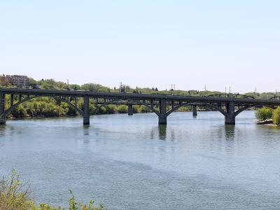 A concrete arch bridge spanning a wide river with urban buildings visible on the left bank and trees lining the riverbanks.
