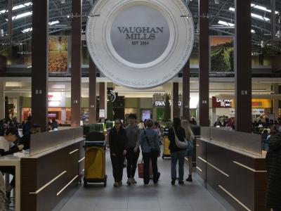 The image shows the interior of a shopping mall food court area, featuring a large circular hanging sign with the text "VAUGHAN MILLS EST 2004" in the center.