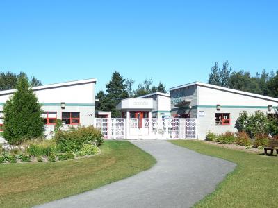 A single-story, modern-style building complex with white siding, green trim, and red window frames, featuring a central gated entrance labeled "ENTRANCE" and a sign on the right wing reading "BIOPARC DE LA GASPÉSIE".