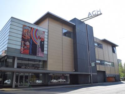A modern multi-story building with a glass and metal facade, featuring large vertical banners on the left side and a prominent "AGH" sign on the roof.
