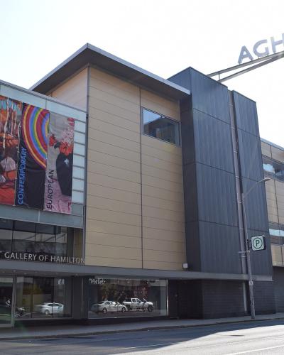 A modern multi-story building with a glass and metal facade, featuring large vertical banners on the left side and a prominent "AGH" sign on the roof.