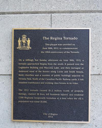 A close-up photograph of a commemorative plaque mounted on a concrete block wall, titled "The Regina Tornado" and detailing the events of June 30, 1912.