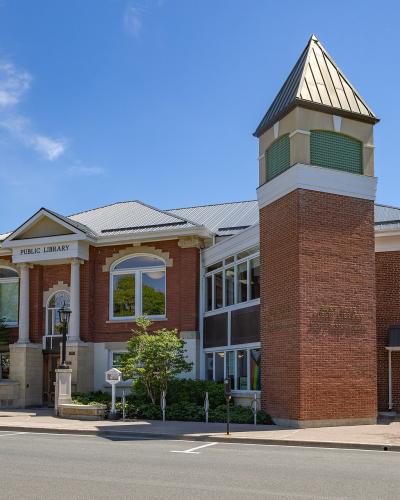 A red brick and stone building with a prominent corner tower, featuring signage reading "PUBLIC LIBRARY" above the main entrance and "PORT HOPE PUBLIC LIBRARY" in raised lettering on the brick tower.