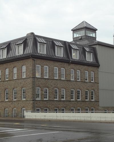 A large stone industrial building with a mansard roof and a water tower in the background displaying the text "SMITHS FALLS".