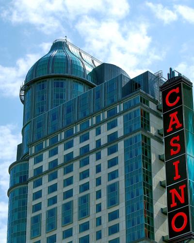 A low-angle shot of a modern high-rise hotel building with a distinctive glass-domed turret and a large vertical red neon sign reading "CASINO" attached to its side against a blue sky.