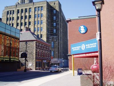 A street-level view of a brick building entrance featuring a blue sign with white text reading "Maritime Museum of the Atlantic" and "Musée Maritime de l'Atlantique," along with the address "1675 Lower Water Street."