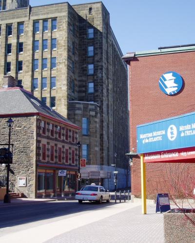 A street-level view of a brick building entrance featuring a blue sign with white text reading "Maritime Museum of the Atlantic" and "Musée Maritime de l'Atlantique," along with the address "1675 Lower Water Street."