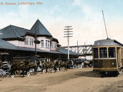 A vintage colorized postcard showing the C.P.R. Station in Lethbridge, Alberta, featuring a large brick train station building with a distinctive turret, horse-drawn carriages, and a streetcar on tracks in the foreground.