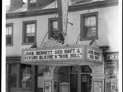 A black and white photograph of a theater facade featuring a large vertical marquee sign reading "CAPITOL" and a horizontal marquee advertising the film "NOB HILL" starring Joan Bennett and George Raft.
