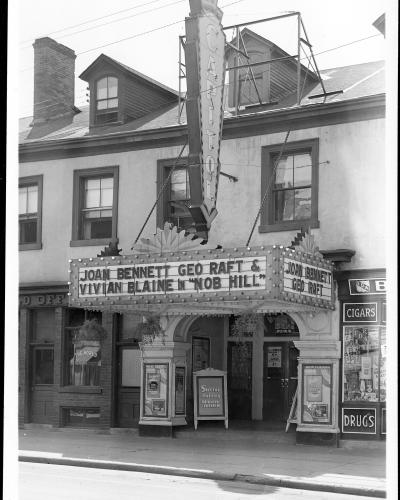 A black and white photograph of a theater facade featuring a large vertical marquee sign reading "CAPITOL" and a horizontal marquee advertising the film "NOB HILL" starring Joan Bennett and George Raft.