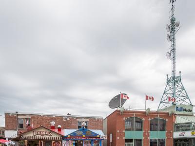 The image shows an outdoor street scene with food kiosks, including a "BeaverTails" stand and a blue "Hot N' Fries" cart, situated in front of brick buildings and a tall telecommunications tower bearing a "Bell Media" sign.