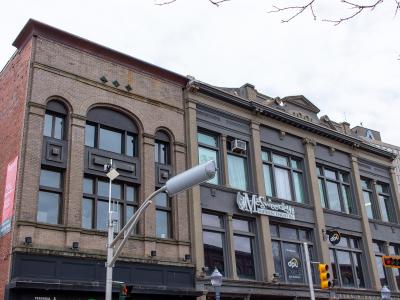 A street-level view of the McSweeney Building, a historic brick and stone structure housing the McSweeney's Dinner Theatre, located on a city street corner with traffic signals and adjacent buildings.