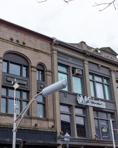 A street-level view of the McSweeney Building, a historic brick and stone structure housing the McSweeney's Dinner Theatre, located on a city street corner with traffic signals and adjacent buildings.