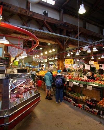 An indoor market scene featuring a meat counter on the left and a produce stand on the right, with a distinctive red curved track running along the ceiling and a "Sunlight Farms" sign visible.