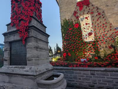 A stone cenotaph covered in red poppies stands in the foreground, with a large stone building behind it featuring a massive poppy installation cascading down its facade.