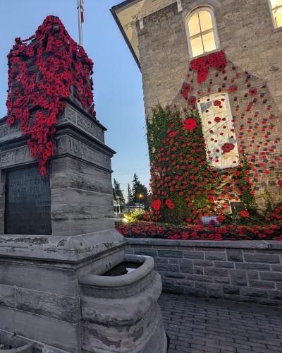 A stone cenotaph covered in red poppies stands in the foreground, with a large stone building behind it featuring a massive poppy installation cascading down its facade.