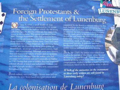 A close-up photograph of a blue informational sign titled "Foreign Protestants & the Settlement of Lunenburg" with a logo for the Town of Lunenburg in the top right corner.