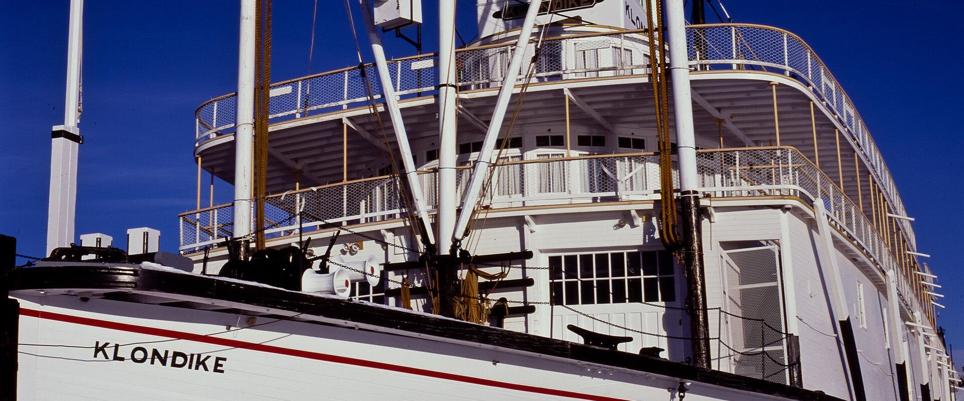 A close-up view of the white hull and upper decks of a historic sternwheeler steamboat named "KLONDIKE" against a clear blue sky.