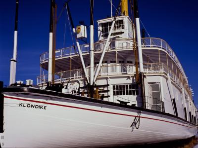 A close-up view of the white hull and upper decks of a historic sternwheeler steamboat named "KLONDIKE" against a clear blue sky.