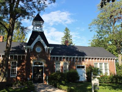 A red brick building with a central cupola and a sign in the front yard reading "MUSEUM" and "ENTRANCE".