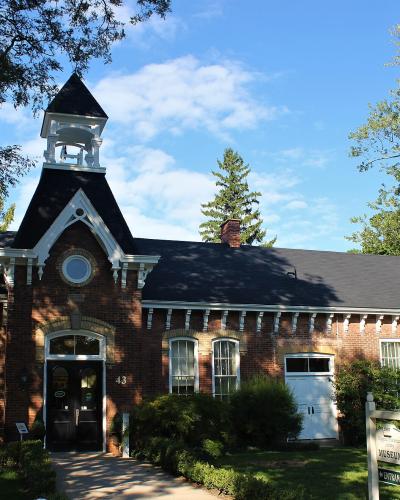 A red brick building with a central cupola and a sign in the front yard reading "MUSEUM" and "ENTRANCE".