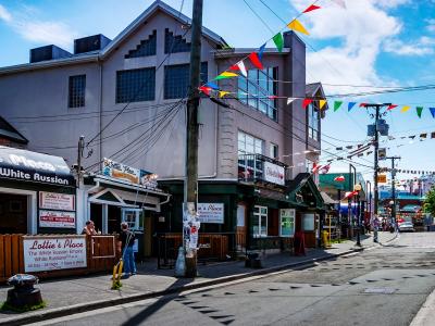 A street scene featuring a pub called "Lottie's Place" with a sign advertising "The White Russian Empire," colorful bunting strung overhead, and a distinctive building with glass block windows on the corner.