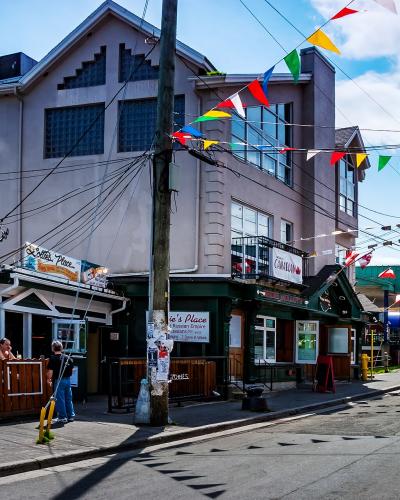 A street scene featuring a pub called "Lottie's Place" with a sign advertising "The White Russian Empire," colorful bunting strung overhead, and a distinctive building with glass block windows on the corner.