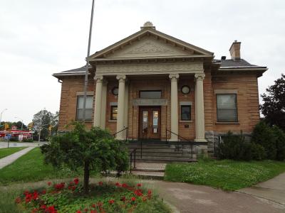 A red brick building with a classical portico featuring four columns and a pediment, with the text "PUBLIC LIBRARY" clearly visible above the entrance doors.