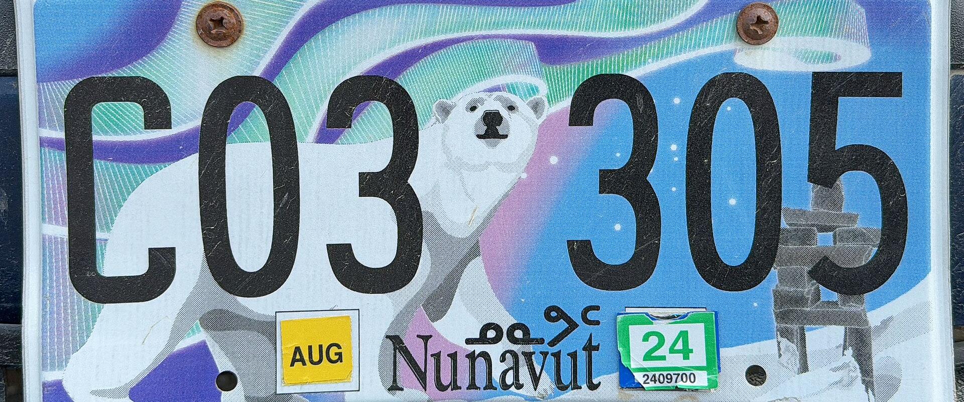 A close-up photograph of a vehicle license plate featuring a polar bear, an inuksuk, and the word "Nunavut" printed at the bottom center.