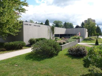 A low-rise concrete building with "GALERIE D'ART MUSÉE ACADIEN" lettering on the facade, surrounded by green lawns and trees.