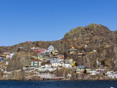 A view of colorful houses built on a steep, rocky hillside overlooking a body of water, with a large rocky peak rising in the background.