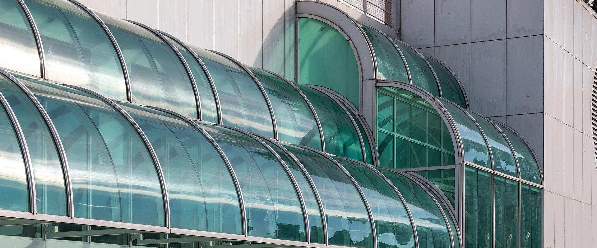 A close-up view of the distinctive curved, green-tinted glass canopy and white facade of a modern building.