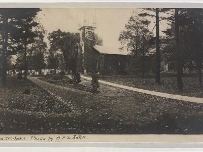 A vintage black and white photograph showing a stone church with a bell tower situated among trees, with a handwritten caption at the bottom reading "St. Mark's Church Niagara-on-the-lake Photo by A.P. St. John."