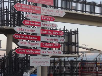 A directional signpost featuring red and white arrows pointing to various global ports and cities, topped with a large red sign reading "St. Catharines Museum Welland Canals Centre St. Catharines, Ontario, Canada".