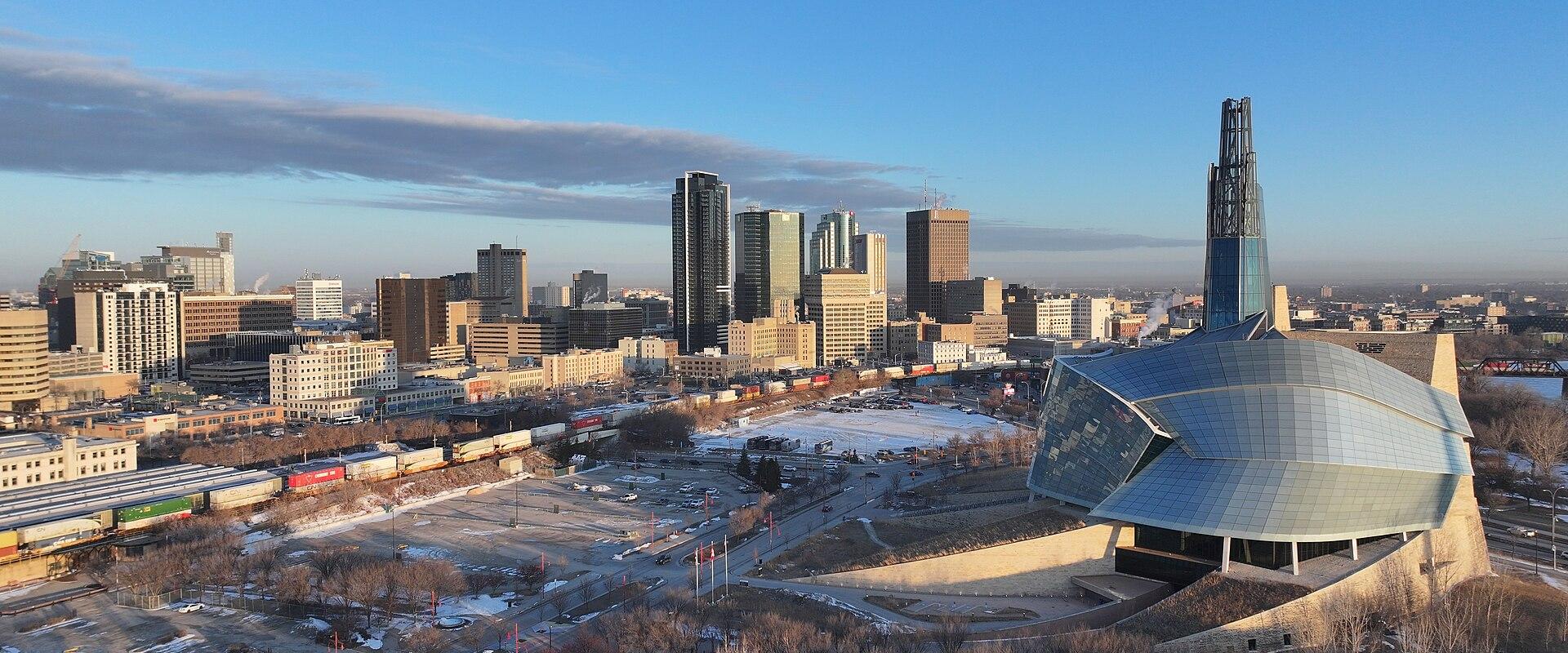 A city skyline featuring a prominent Canadian flag in the foreground, a CN freight train on tracks, and several high-rise buildings including one with a TD Bank logo.