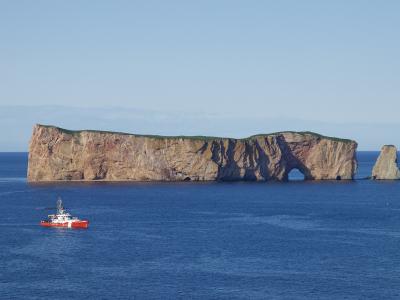 A large, flat-topped limestone sea stack with a prominent natural arch at its base, situated in the ocean with a small red and white boat in the foreground.