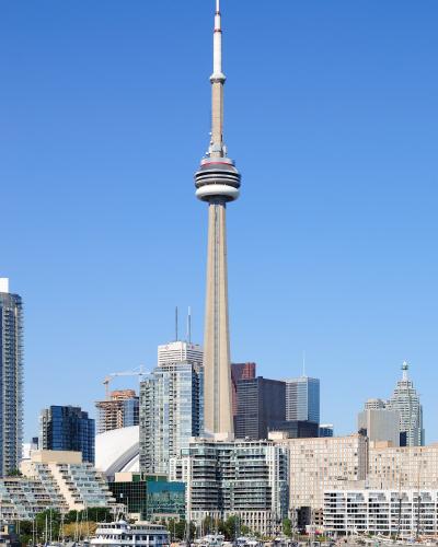 The image shows the CN Tower and the Toronto skyline viewed from the water, with a white tour boat docked at the harbourfront in the foreground.