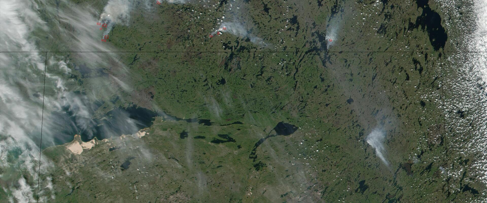 A satellite image showing a large area of boreal forest and wetlands with multiple active wildfires (indicated by red hotspots and white smoke plumes) and scattered clouds.