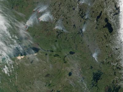 A satellite image showing a large area of boreal forest and wetlands with multiple active wildfires (indicated by red hotspots and white smoke plumes) and scattered clouds.
