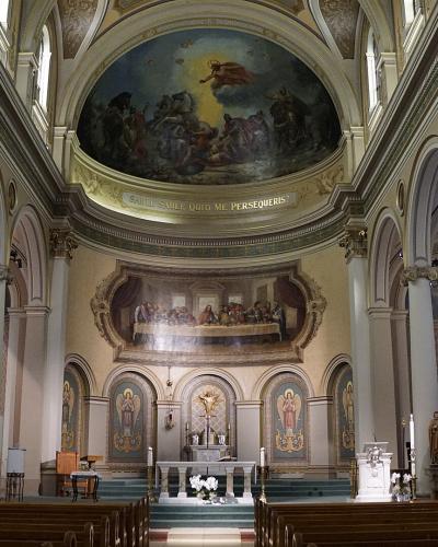 The interior of a historic church featuring a barrel-vaulted ceiling with a large fresco, a mural of the Last Supper above the altar, and a Latin inscription reading "SALE SALIS QUOD ME PERSEQUERIS".