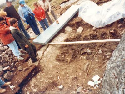 A group of people observing an archaeological excavation site where a large whale skeleton is being uncovered in the earth.
