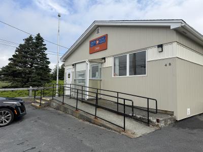 A beige, single-story Canada Post building with a ramp and railing, featuring a sign that reads "CANADA POST / POSTES CANADA" and "Dildo" below it.
