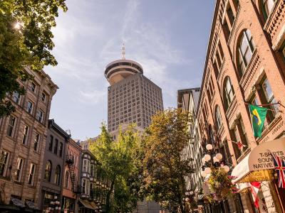 A low-angle street view of historic brick buildings and cobblestones with the distinctive Vancouver Lookout tower rising in the background.